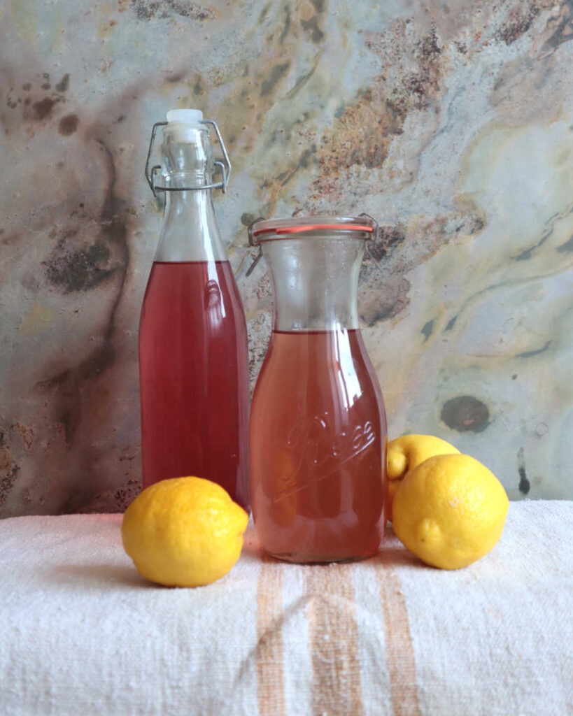 2 Flaschen Fliedersirup vor einem Küchenhintergrund, mit Zitrone