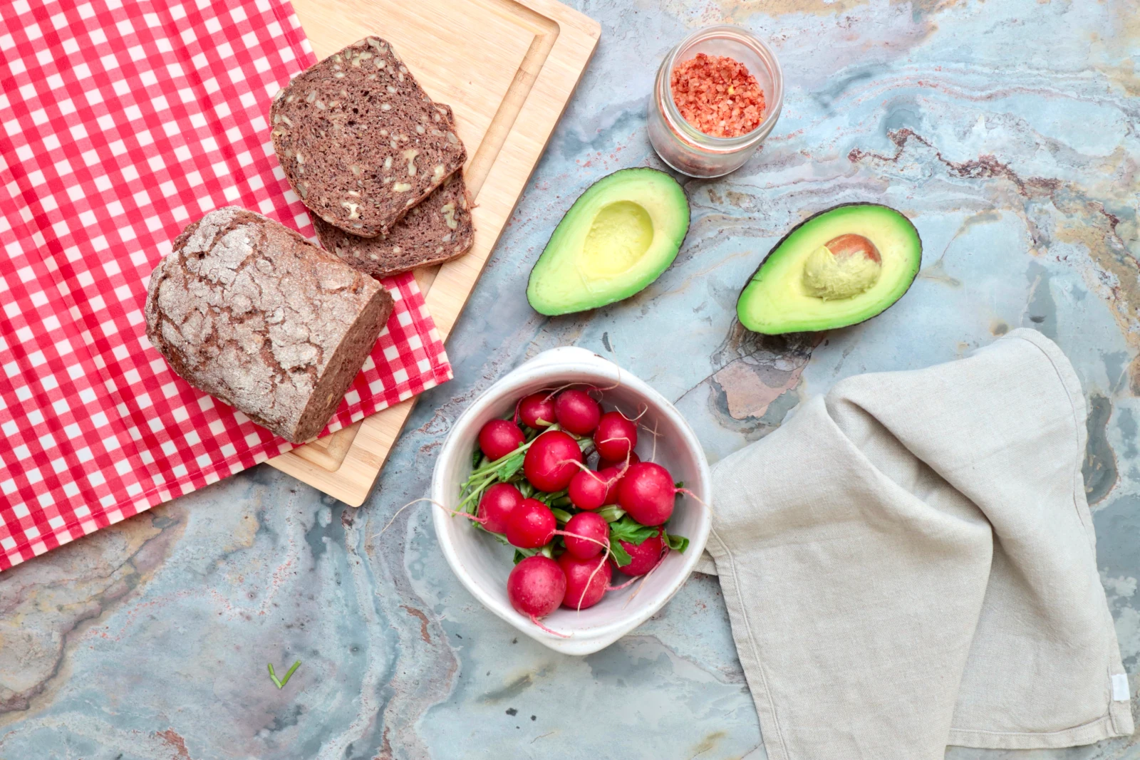 Brotscheiben auf ro kariertem Bienenwachstuch neben Radieschen und Avocado