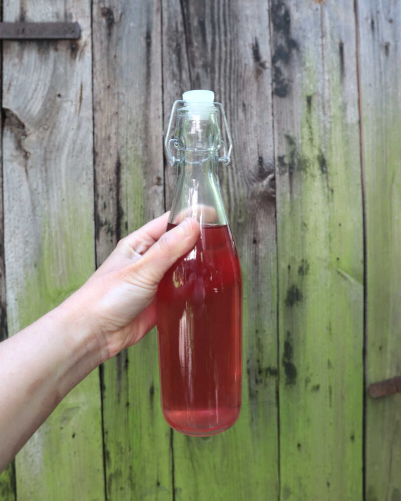 Hand hält Sirupflasche vor Holztor