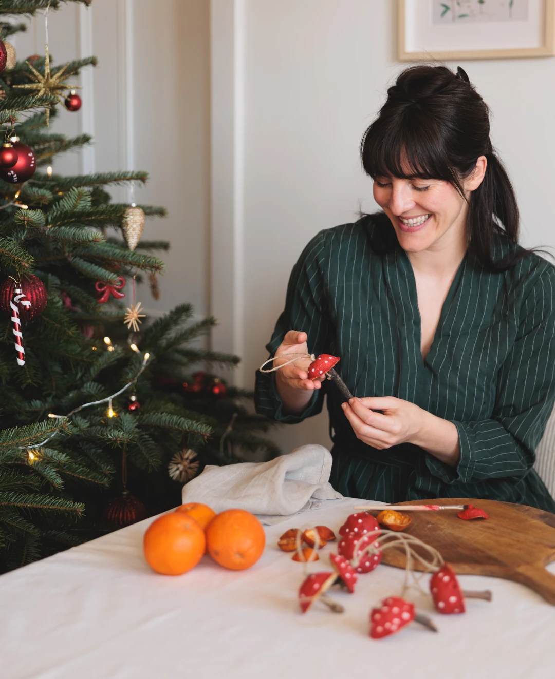 Lächelnde Frau neben Weihnachtsbaum beim Deko basteln